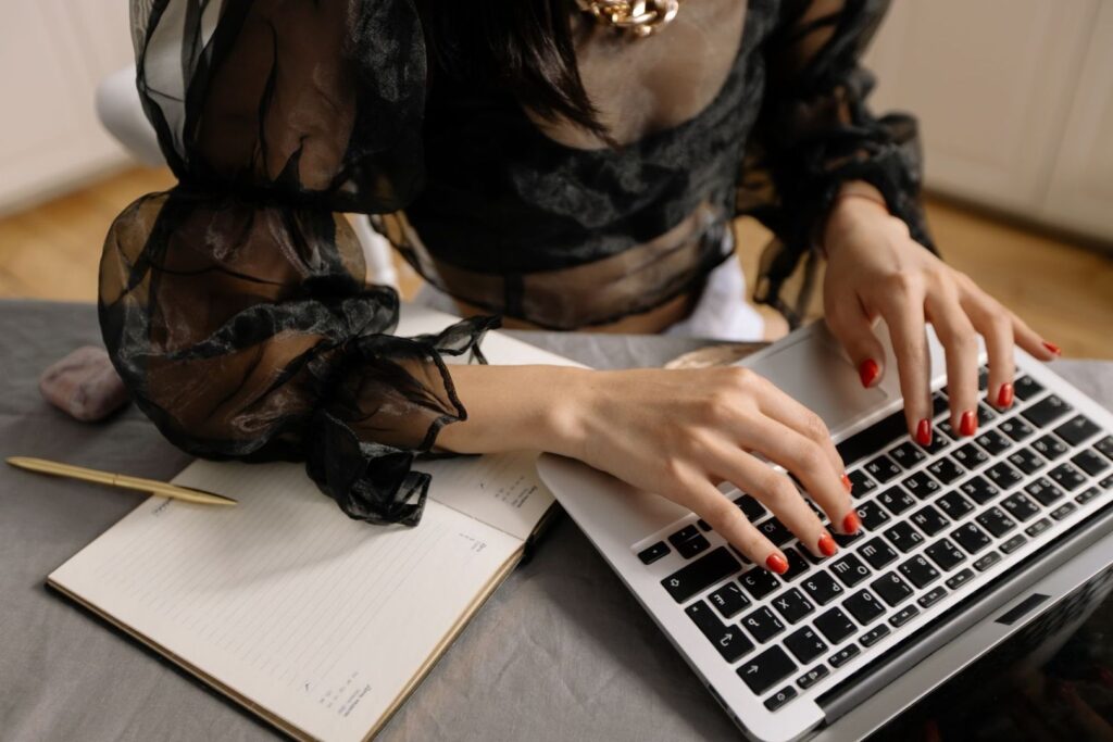 Person i svart blus arbetar vid laptop med anteckningsbok och penna