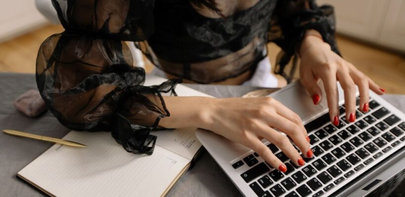 Person i svart blus arbetar vid laptop med anteckningsbok och penna