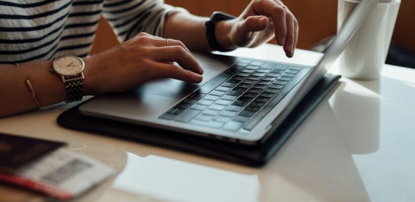 Person arbetar vid en bärbar dator med anteckningsbok bredvid