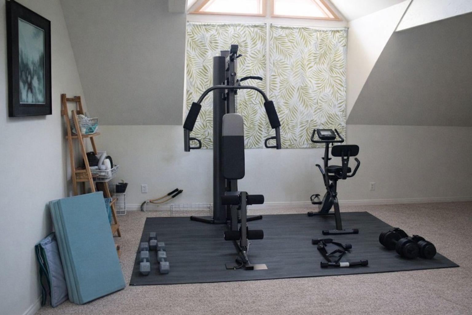 Ett välorganiserat hemmagym i ett ljust vindsrum med träningsmaskiner och fria vikter.